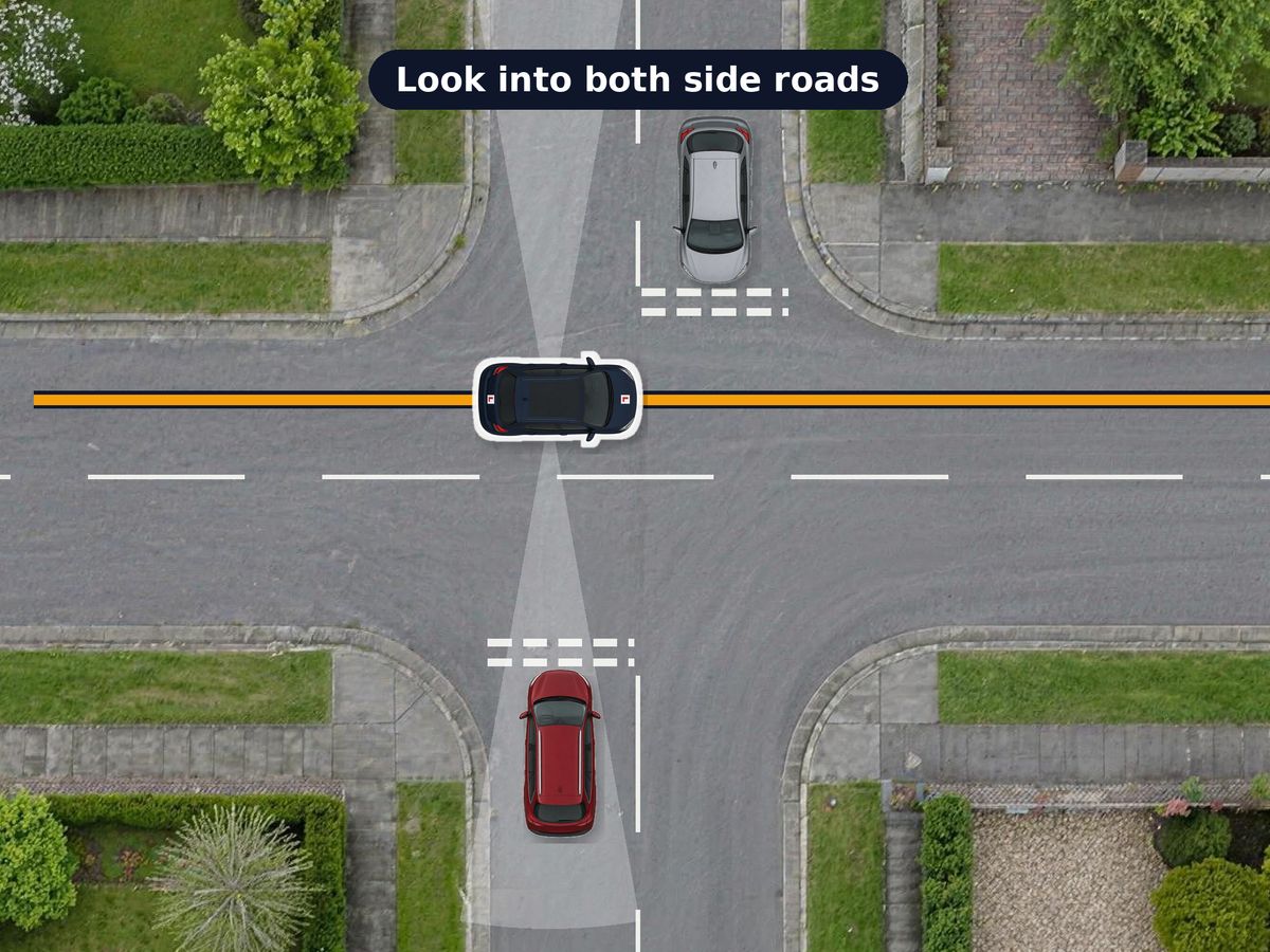 A crossroads from above. The car drives straight along the main road, looking into the side roads on both sides, where a car waits at the give way lines in each.